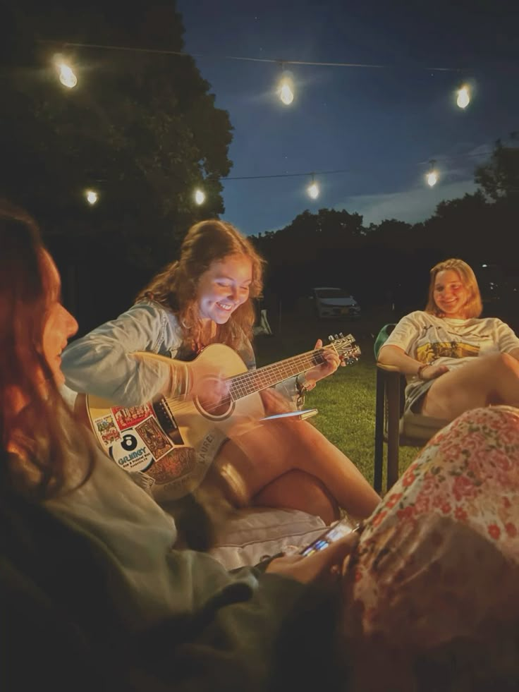 Group of people sitting outside, one girl smiling while playing a guitar