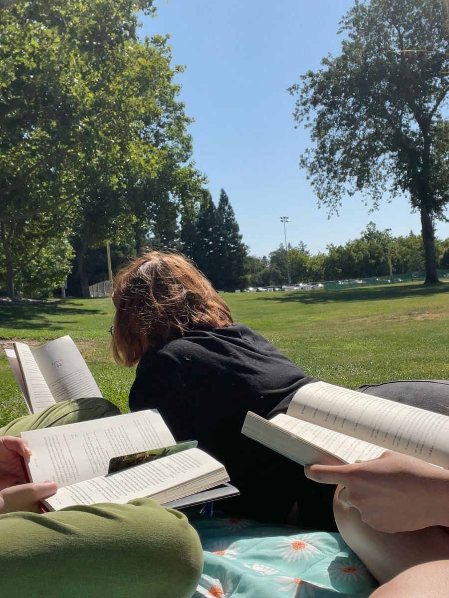 People reading books while lying on the grass in a sunny park